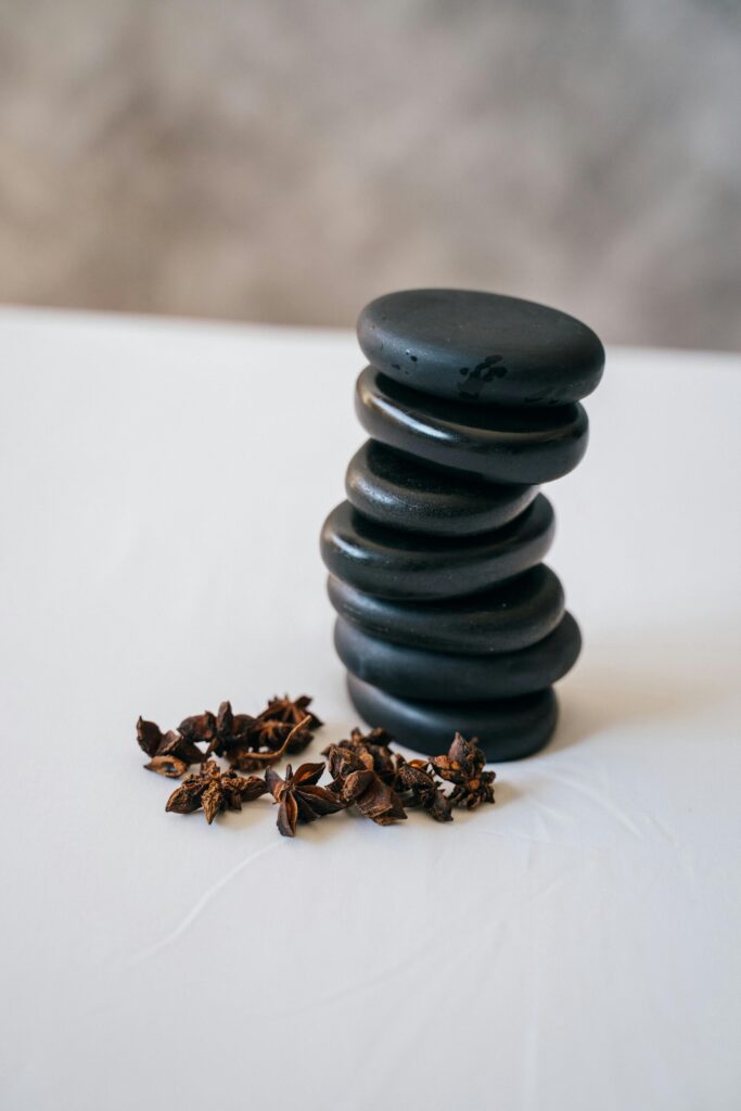 A neat stack of black stones next to a scattering of star anise on a smooth white surface.